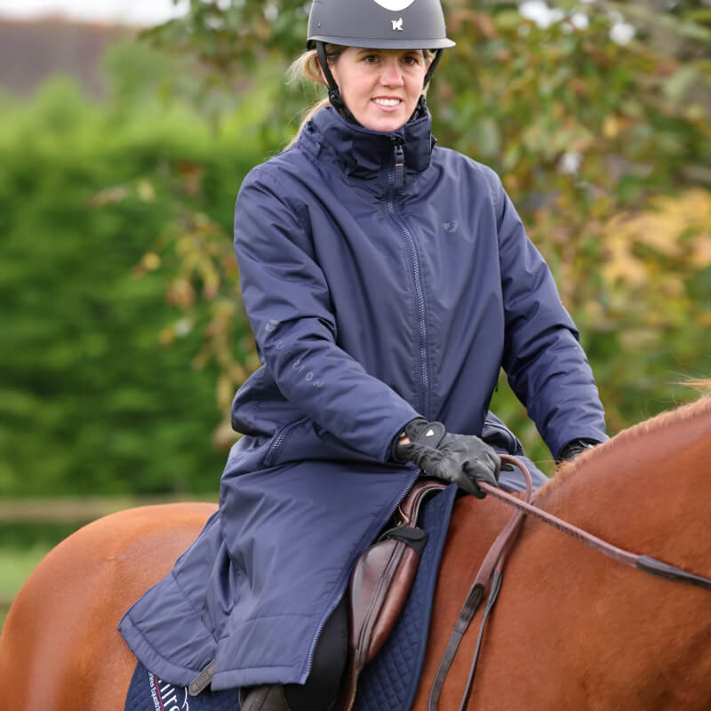 A person in an Aubrion Core All Weather Robe Unisex Navy rides a brown horse outdoors.