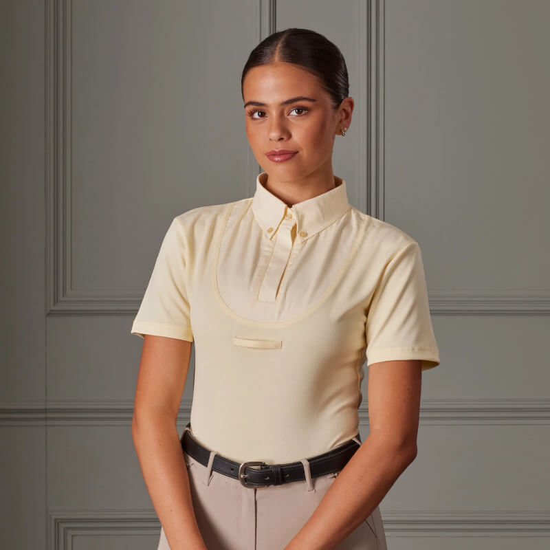 Woman in an Aubrion Short Sleeve Tie Shirt Yellow and beige pants stands by a gray paneled wall.