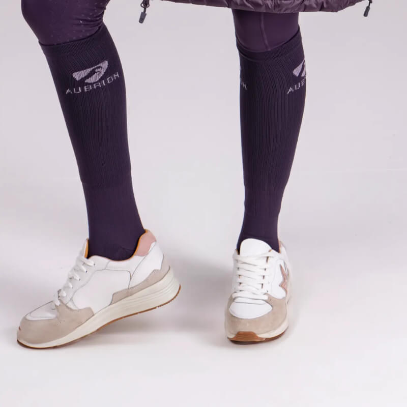 Person wearing Aubrion Winter Performance Socks Adult Purple with logo, standing on a white floor.