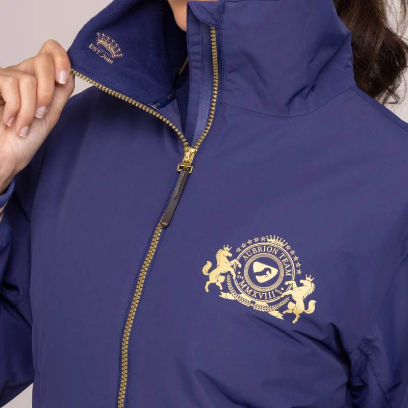 Person wearing an Aubrion Team Blouson Midnight jacket with gold crest and embroidered details.