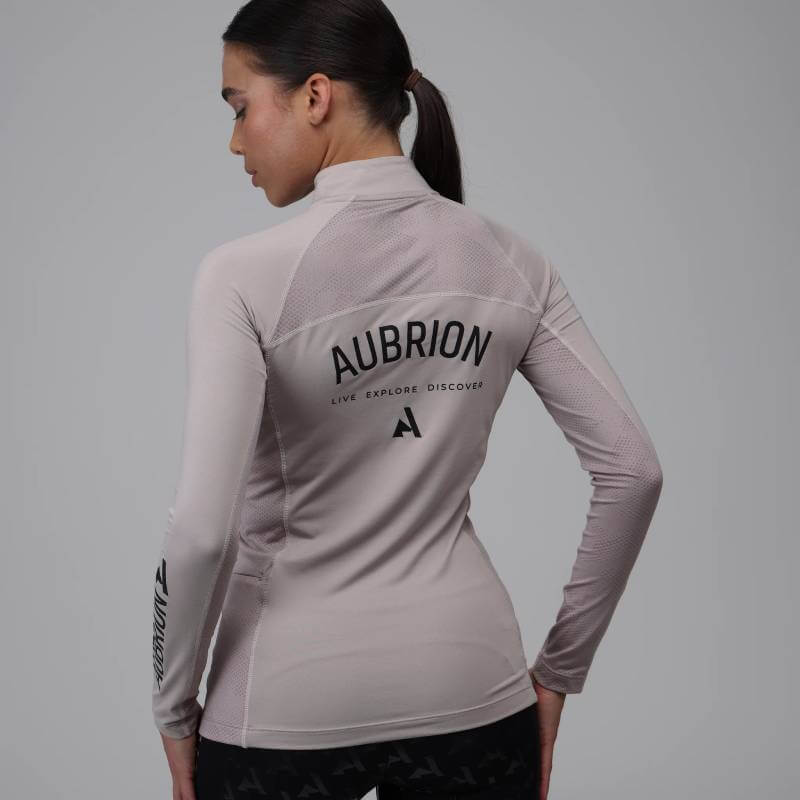 Woman in Aubrion React Long Sleeve Baselayer Sand with "AUBRION" on back, facing away.