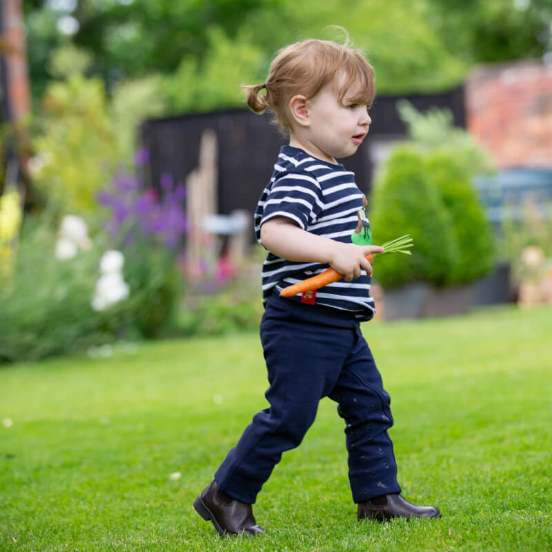 Toddler in Shires Winnie & Me Childs Jodhpurs Navy walks on grass holding a carrot.