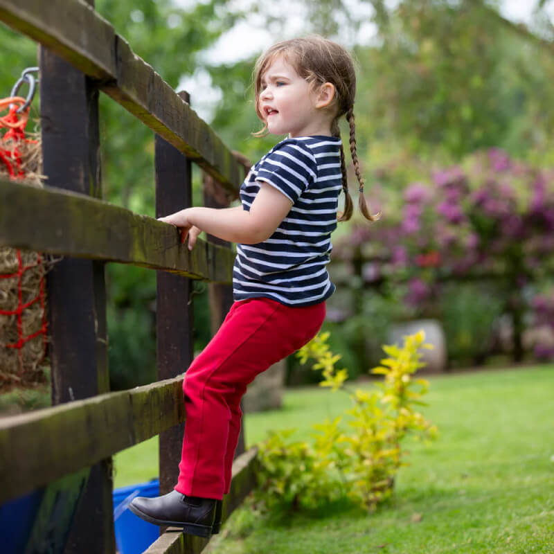 Young girl in Shires Winnie & Me Childs Jodhpurs Red climbs a wooden garden fence.