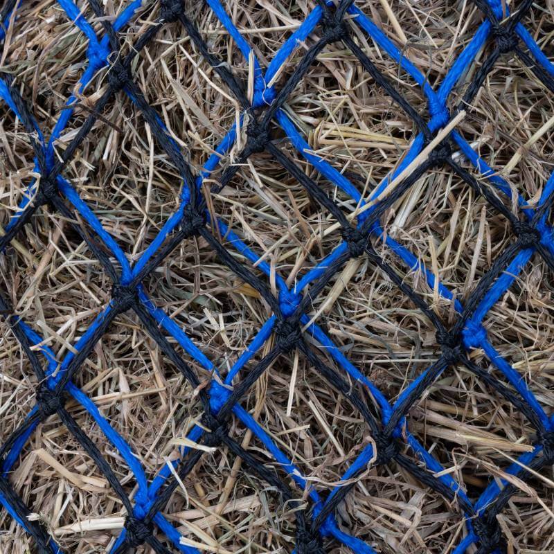 Close-up of dry hay behind Shires Greedy Feeder Duo 1.5" Haynet Black/Blue 40" for controlled feeding.
