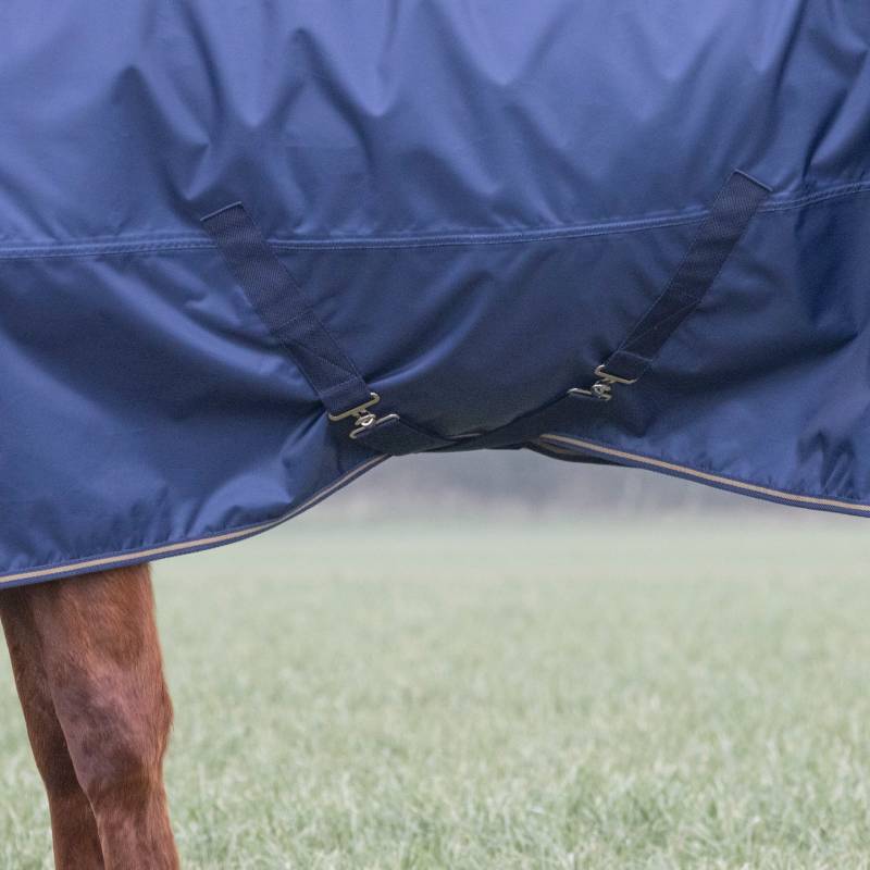 A horse wears the Shires Typhoon Light Turnout Rug Navy, standing on grass.