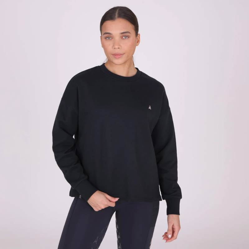 Woman in a Shires Aubrion React Sweatshirt Shadow and leggings stands against a light background.