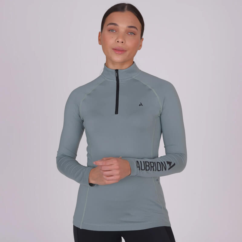 Woman in Aubrion React Winter Baselayer Sage top with logo on the left sleeve.