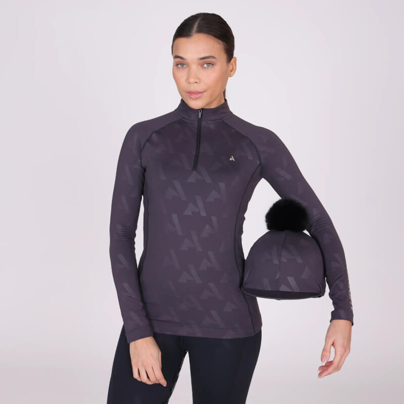 Woman in Aubrion React Winter Baselayer Shadow holding matching beanie with black pom-pom.