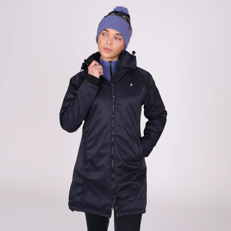 Woman in a Shires Aubrion React Mid Length Coat Shadow and blue beanie poses hands in pockets.
