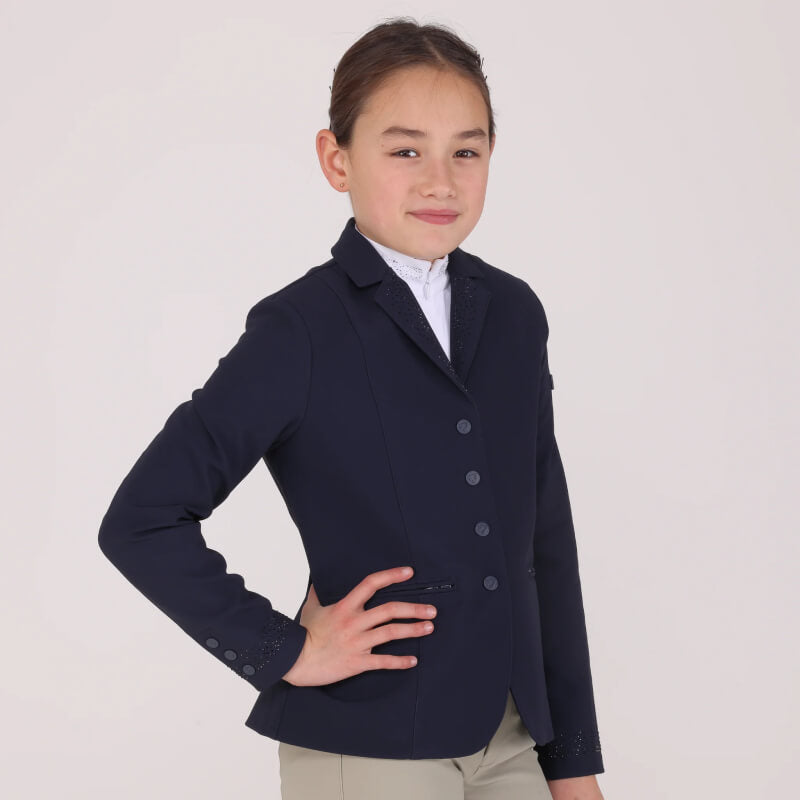 Young rider wears the Shires Aubrion Optima GX Show Jacket in navy, smiling with hand on hip.