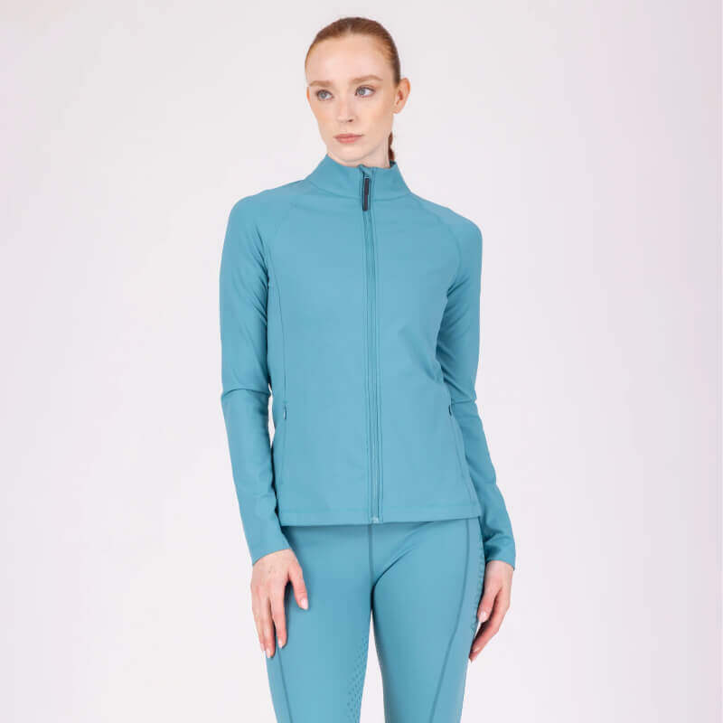 A woman in the Aubrion React Mid Layer Haze stands against a plain background, exuding comfort.