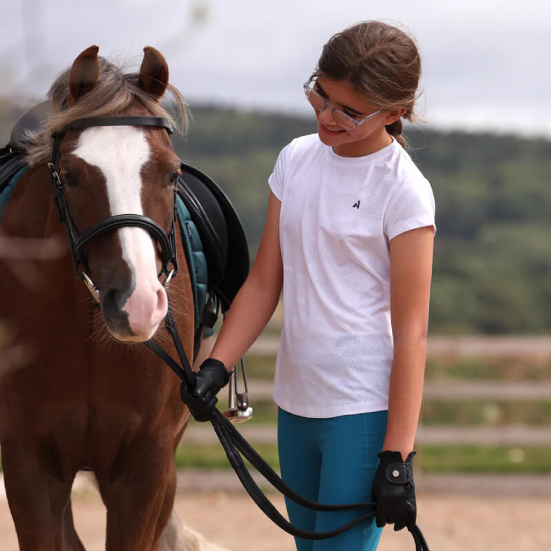 Girl in Aubrion React Young Rider Tech T-Shirt White smiles at a brown horse with white stripe.