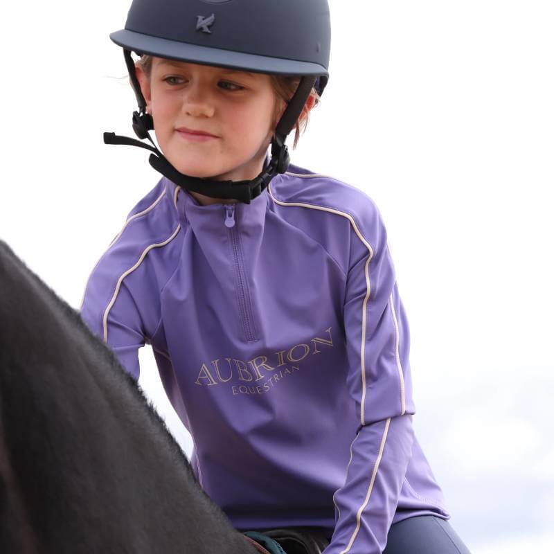 Young rider in Aubrion Heather Long Sleeve Baselayer and helmet riding a horse.