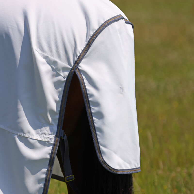 A horse in a Shires Highlander Plus Sweet-Itch Combo Neck Fly Rug White/Air Force stands on grass.