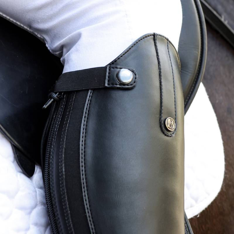 Close-up of black Brogini Modena Synthetic Long Boot Wide in a stirrup on a white saddle pad.