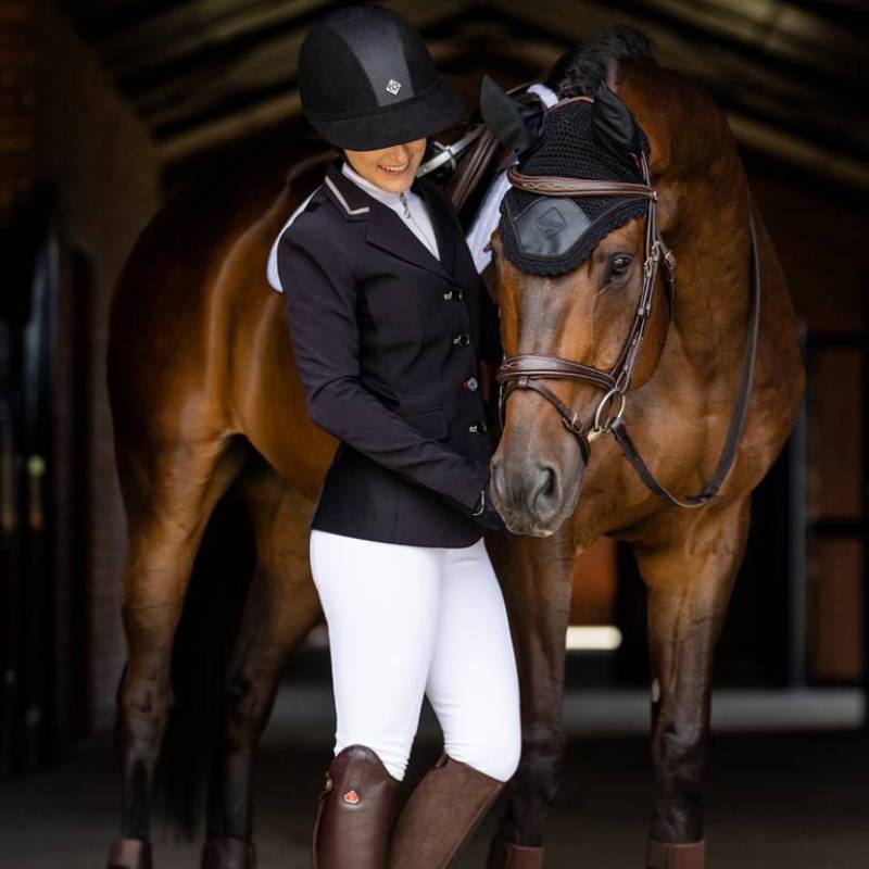 Equestrian in riding gear stands by a brown horse in a LeMieux Acoustic Pro Fly Hood Black.