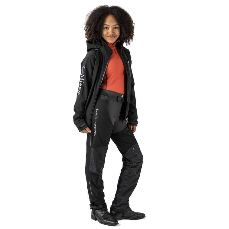 Smiling girl in LeMieux Junior Drytex Stormwear Waterproof Chaps and a red top.