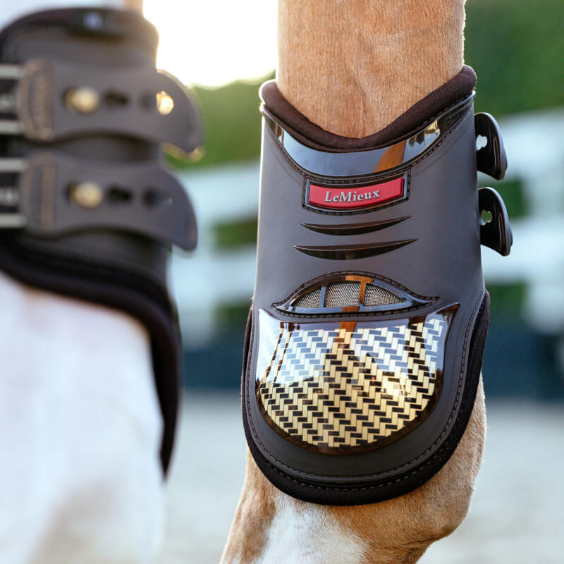 Close-up of horse's leg wearing LeMieux Exo-Flex Fetlock Boot Brown/Gold for tendon protection.