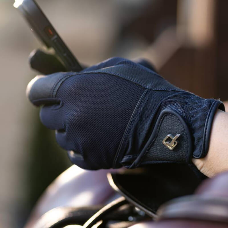 A gloved hand holding a smartphone, featuring LeMieux Pro Mesh Glove Navy’s textured fabric.