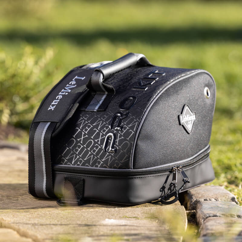 LeMieux Elite Pro Hat Bag Black with zippers and strap, outdoors on stone with grass behind.