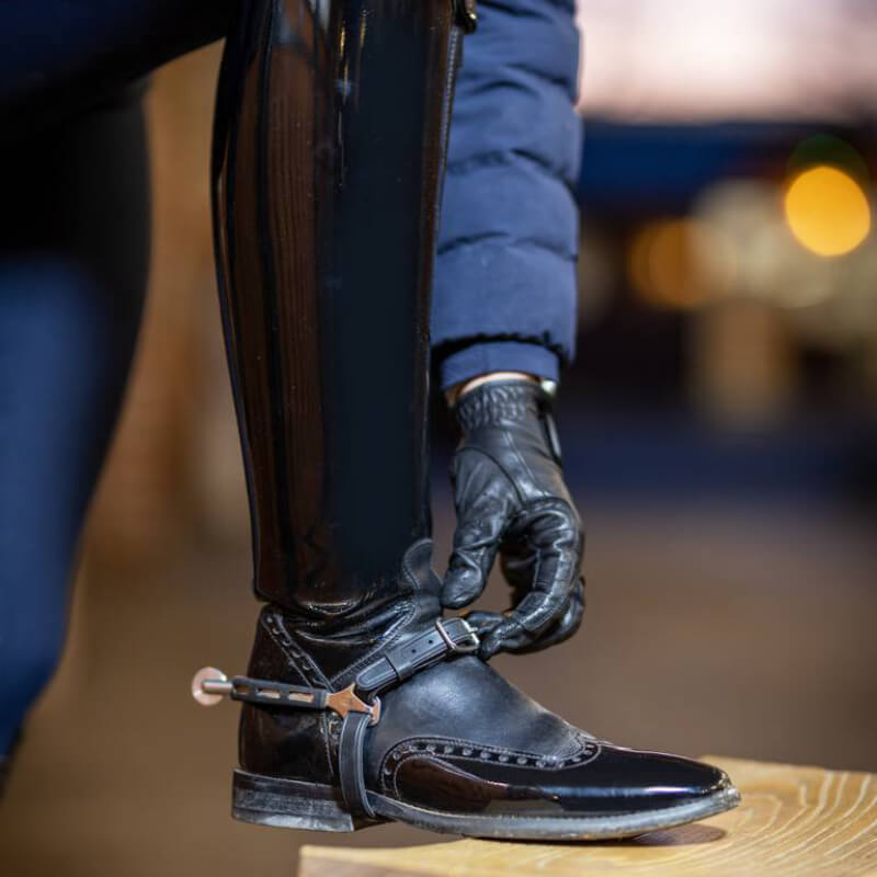 A person fastens LeMieux Spur Straps Black by LeMieux to their riding boots.