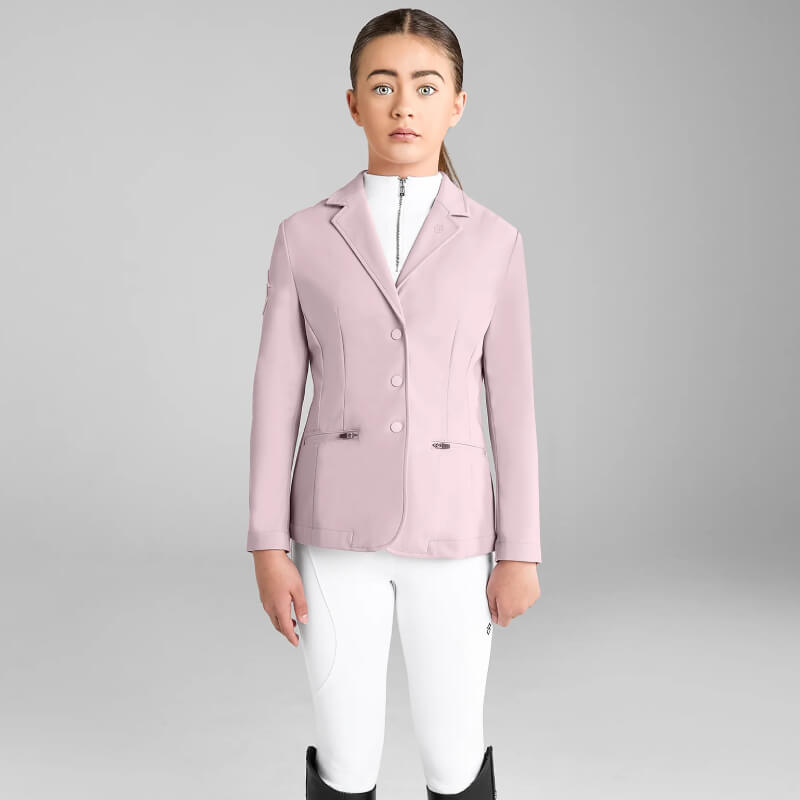 Girl wears Aztec Diamond YR Competition Jacket Pink, white pants; stands by a plain gray background.