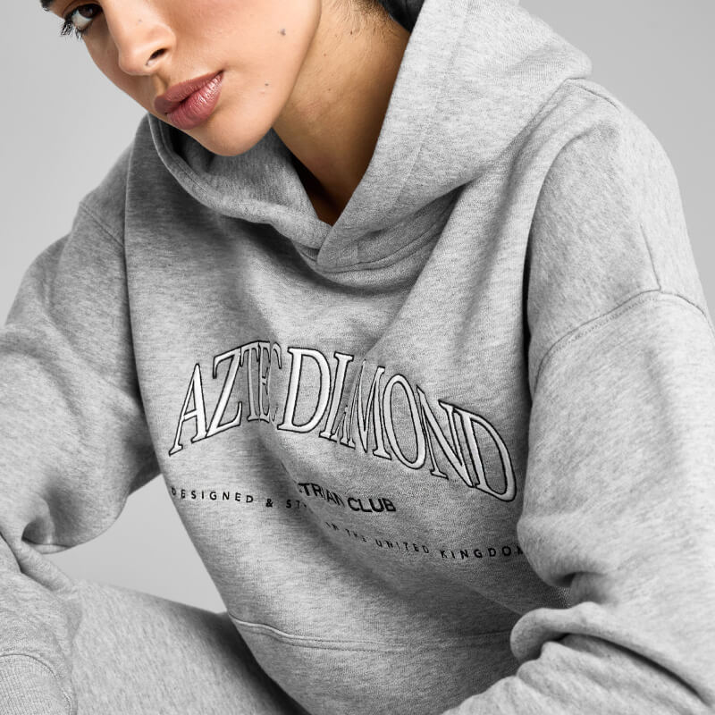 Woman in Aztec Diamond EQ Club Pull On Hoodie Grey Marl, sitting indoors.
