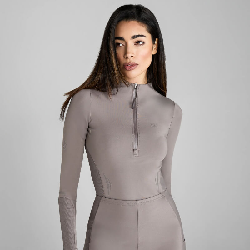 Woman in Aztec Diamond Define Baselayer Truffle set, zip-up top and pants, on gray background.