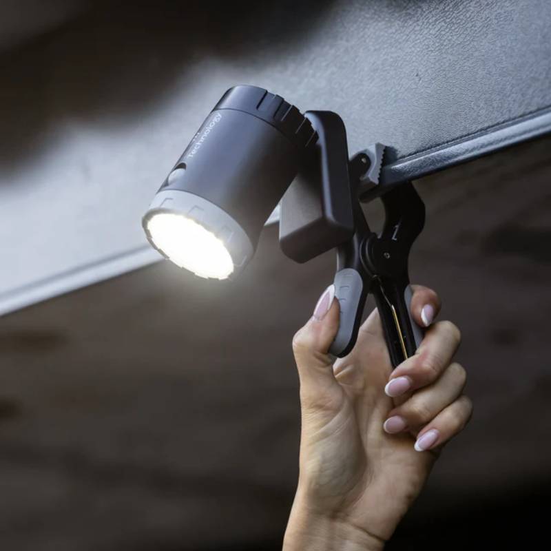 A hand clamps the Woof Wear Multi-Mount LED Work Light Black onto a metal surface.
