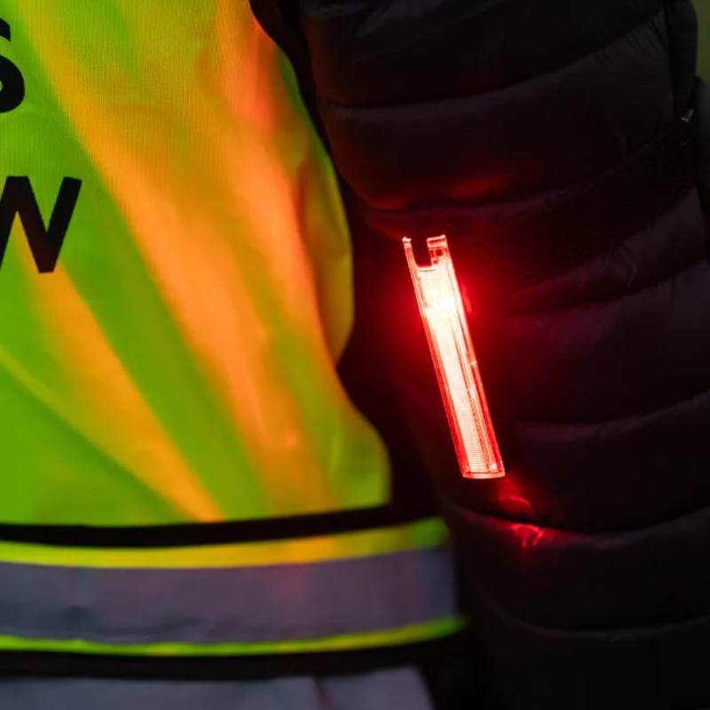 Close-up of a yellow vest and Woof Wear LED 3-in-1 Rider Safety Lights glowing red on an arm.