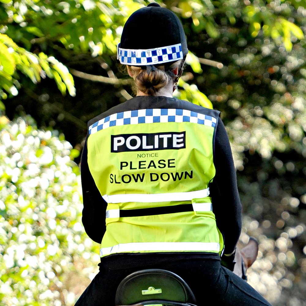 Equisafety Polite Air Waistcoat wearer reads SLOW DOWN sign while riding a horse outside.