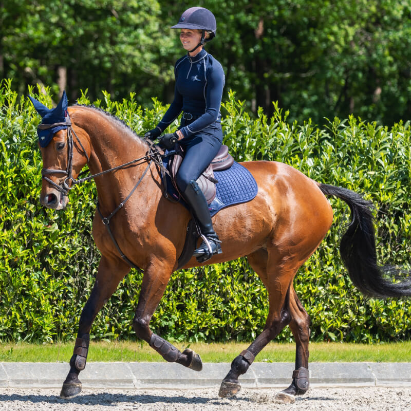Person rides a brown horse outdoors with a LeMieux Suede Close Contact Square Navy saddle pad.