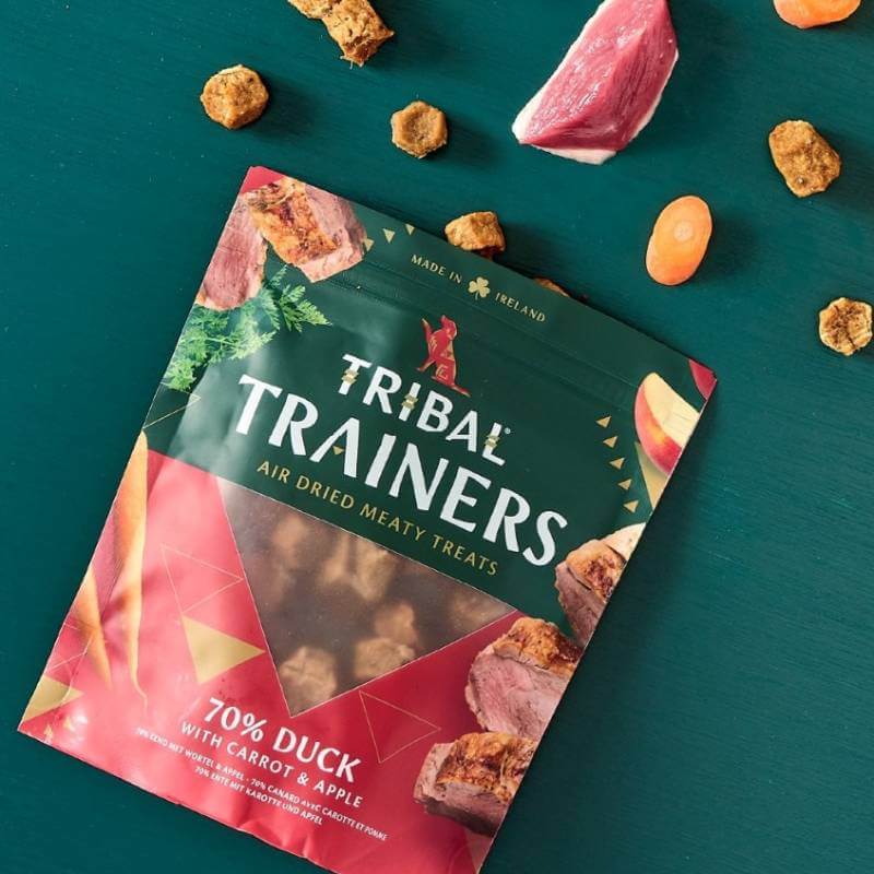 Tribal Trainers Dog Treats Duck, Carrot &amp; Apple 80g scattered with treat pieces.