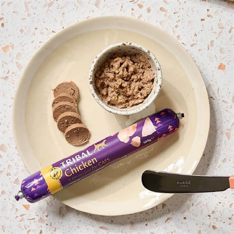 A plate with sliced Tribal Cat Sausage 100g, a bowl of cat food, and a knife.