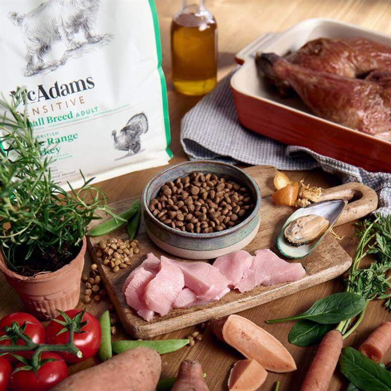 McAdams Dry Dog Food Small Breed Turkey Sensitive on a wooden table with vegetables and herbs.