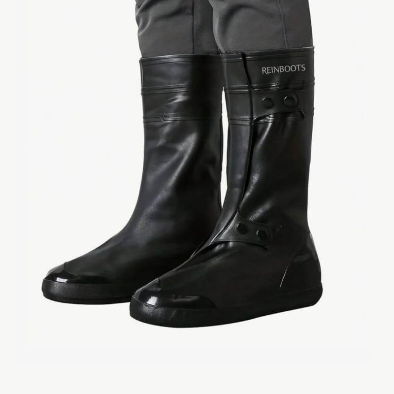 Person wears black silicone Reinwear rain boots over gray pants, labeled Reinboots Black.