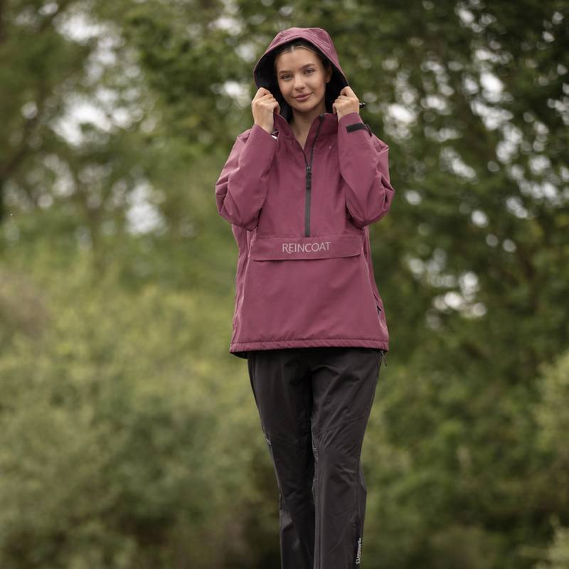 Woman outdoors in Reinwear Reincoat Smock Lite Adult Bloom, adjusting hood over black pants.