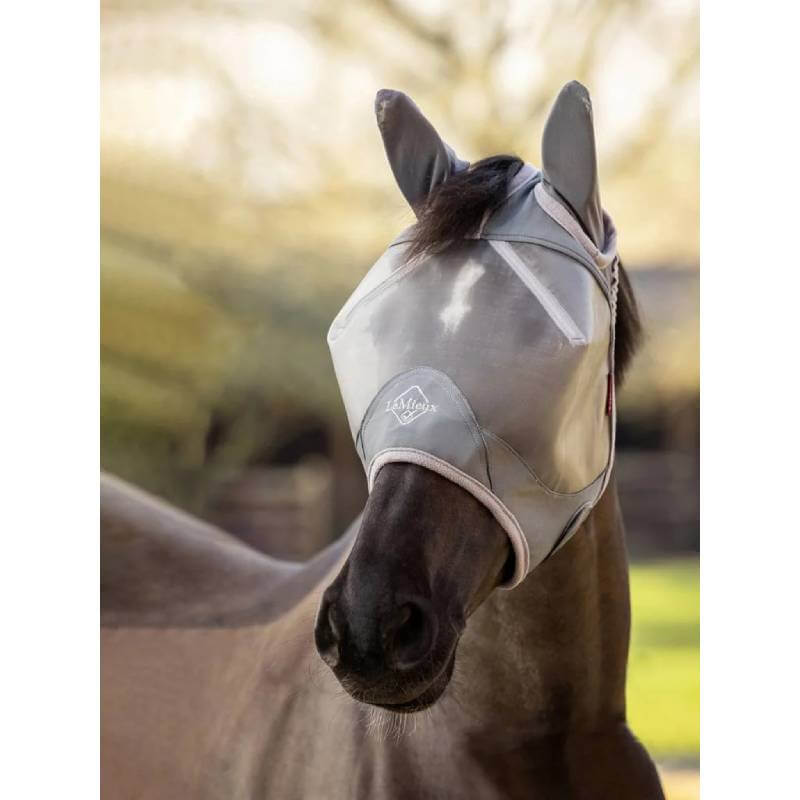 A horse outdoors wears a LeMieux Armourshield Pro Half Fly Mask Grey over its face and ears.