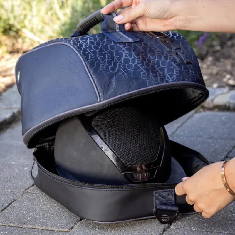 Hands placing a helmet into a LeMieux Elite Pro Hat Bag Navy by LeMieux on a stone path outdoors.