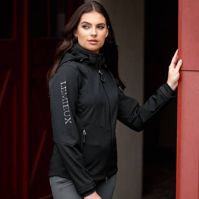 Woman in a LeMieux Celine Soft Shell Jacket Black stands by a red door.