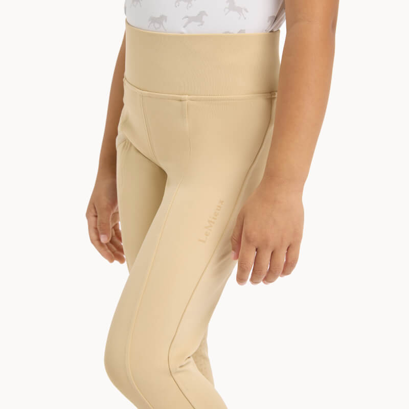 Child in LeMieux Mini Pull On Breech Beige, sweat-wicking leggings, white horse print shirt.