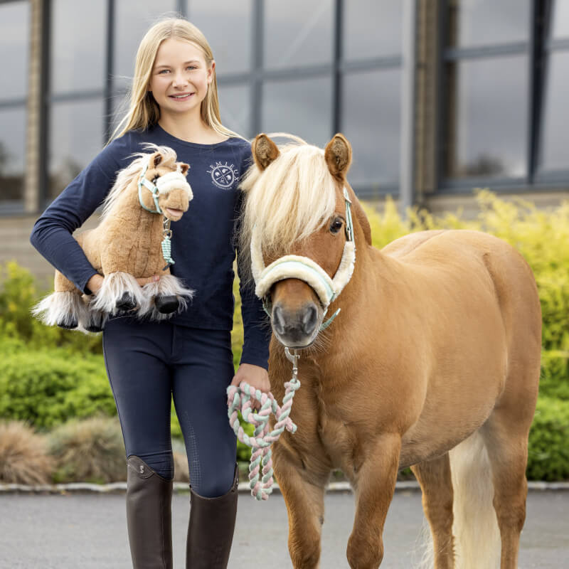 Smiling girl leads a real pony outside, holding the LeMieux Toy Pony Cloudy.