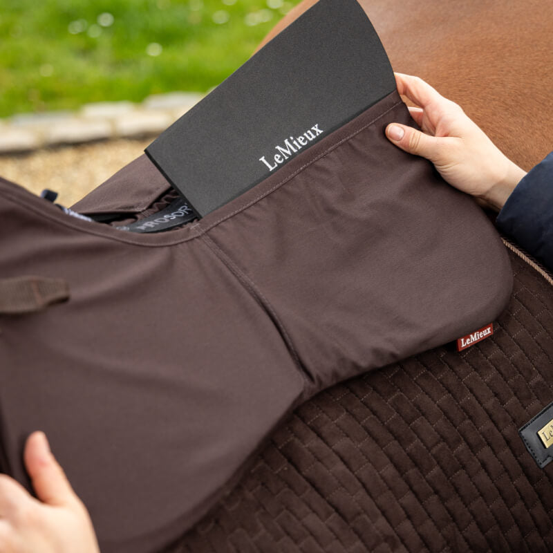 Hands placing a LeMieux ProSorb Plain 2 Pocket Half Pad Brown into a horse’s back pad.