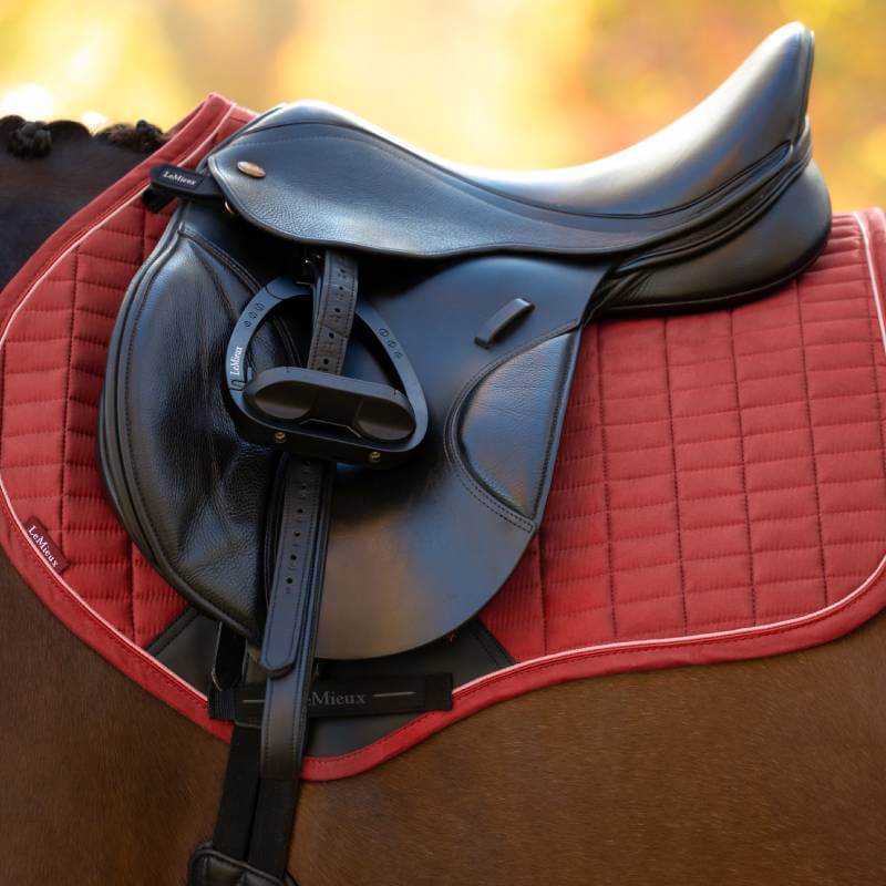 Black English saddle on a LeMieux Suede Close Contact Square Russet, atop a brown horse.
