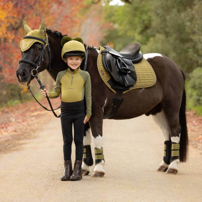 Smiling child in riding gear stands by a horse with a LeMieux Suede Close Contact Square Gooseberry.