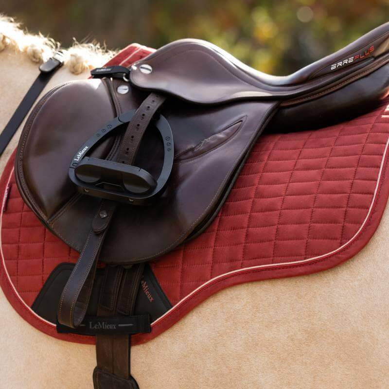 A brown saddle on a LeMieux Suede GP Square Russet pad by LeMieux, shown close-up on a horse.