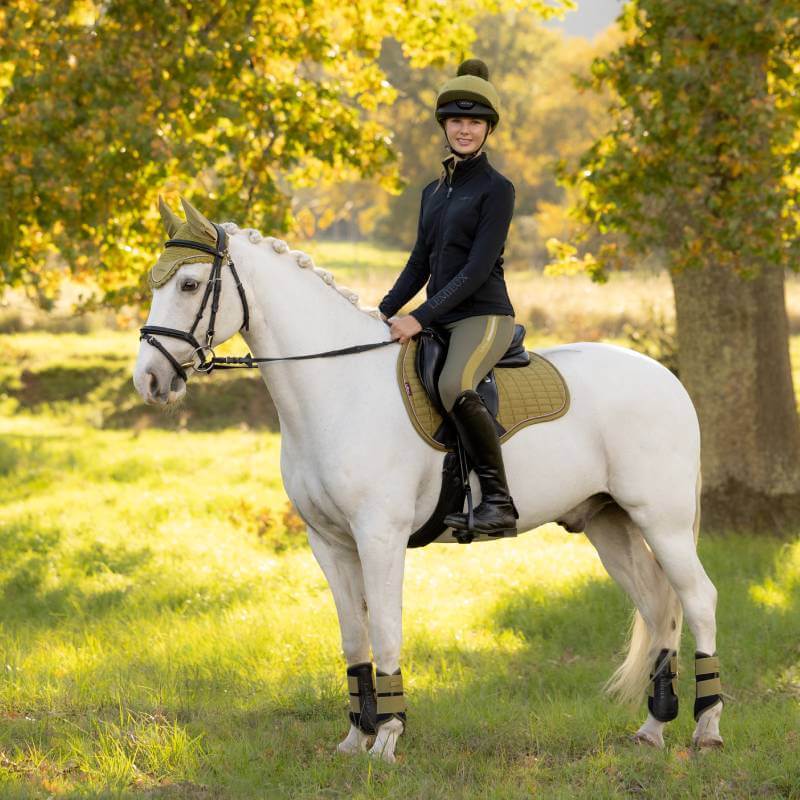 Rider on white horse with LeMieux Suede GP Square Gooseberry in a grassy field.