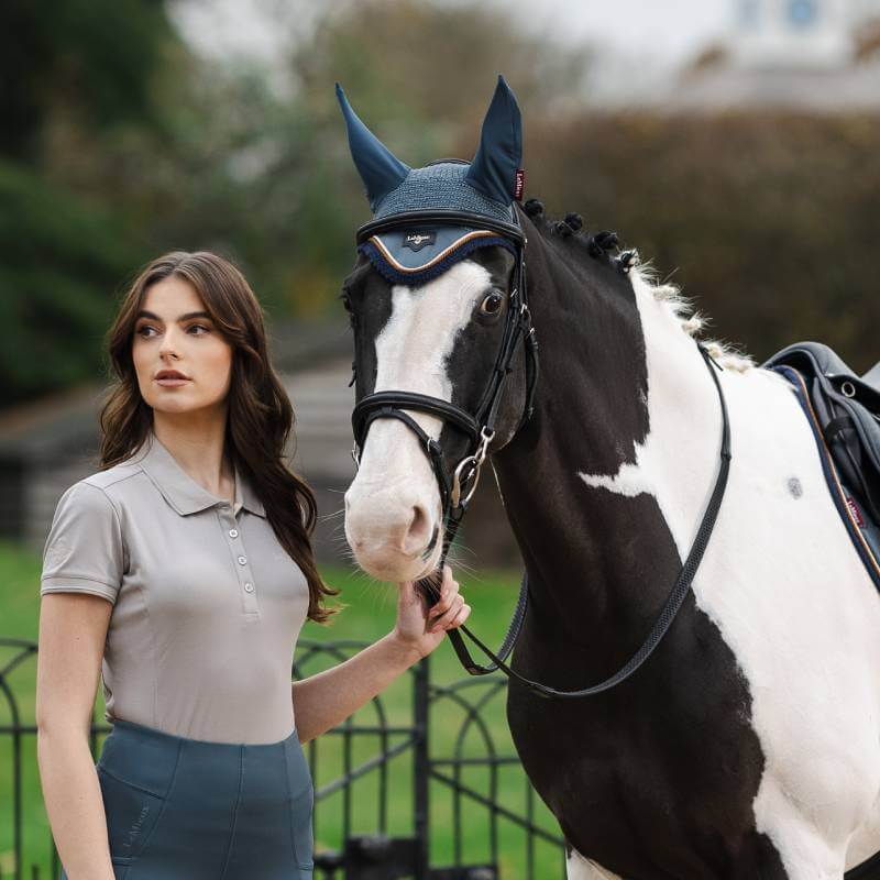 Woman stands beside black and white horse in LeMieux Loire Fly Hood Petrol.