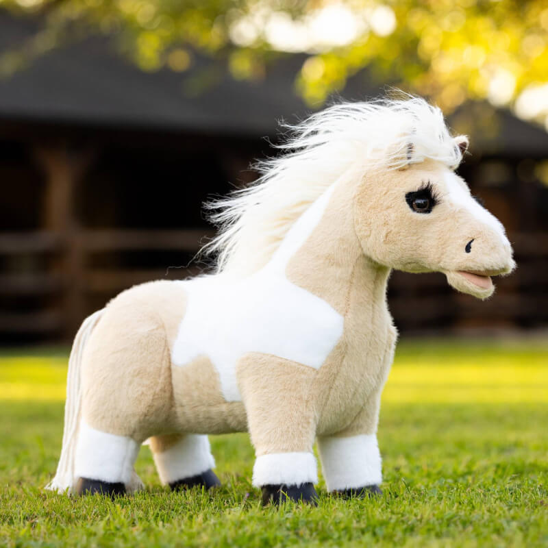 A LeMieux Lemieux Toy Pony Lemon with white and tan fur stands on green grass outdoors.