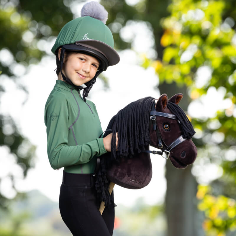 Smiling child in riding gear holds a LeMieux Hobby Horse Freya outdoors.